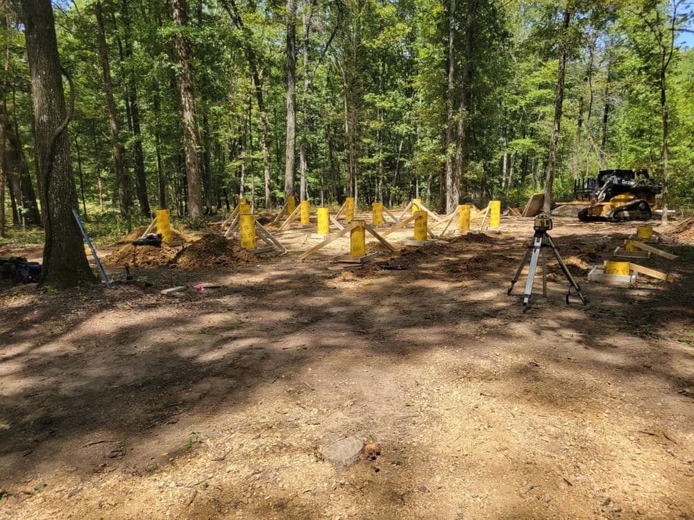 Construction site in a forest clearing with yellow markers and surveying equipment.