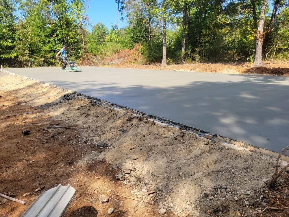 Concrete pouring process on a construction site in a wooded area with a worker using machinery.