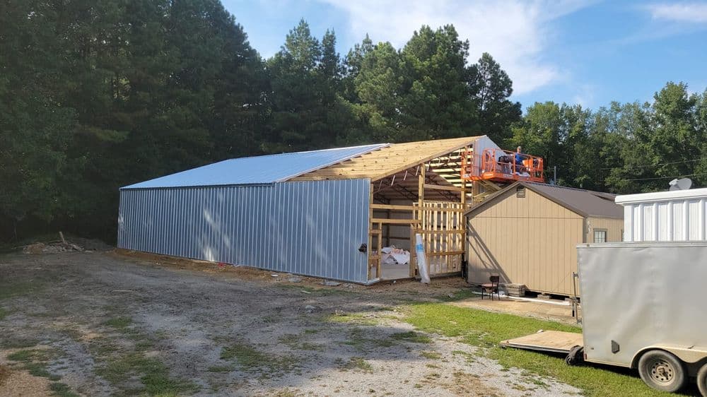 Construction of a barn with a metal roof and wooden frame in a wooded area.