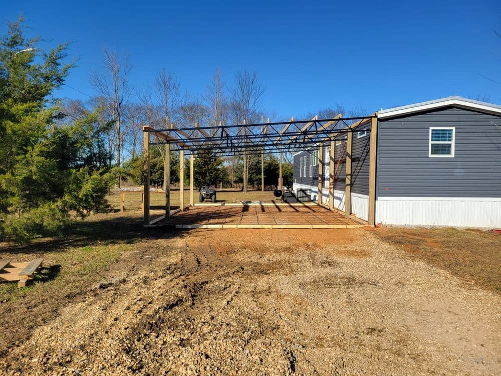 Wooden structure framing an outdoor patio next to a mobile home on clear blue sky day.