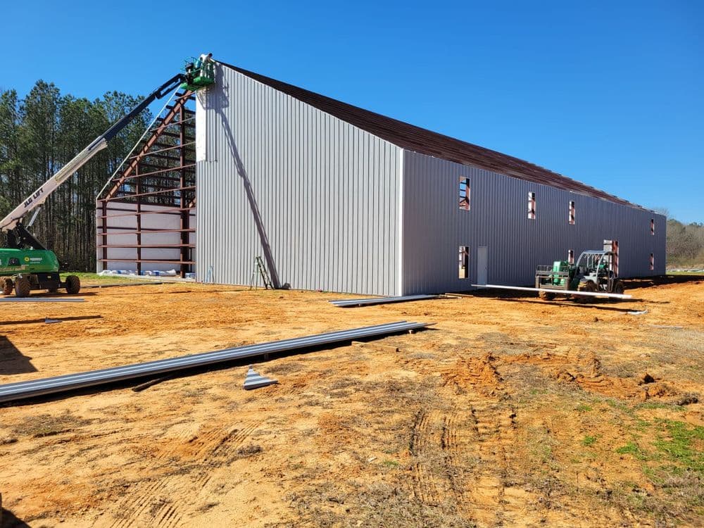 Construction of a metal building with cranes and equipment on a sunny day.