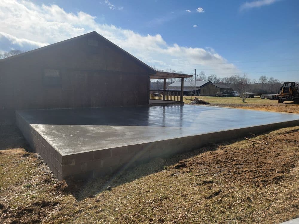 Concrete slab foundation adjacent to a wooden building under a clear blue sky.