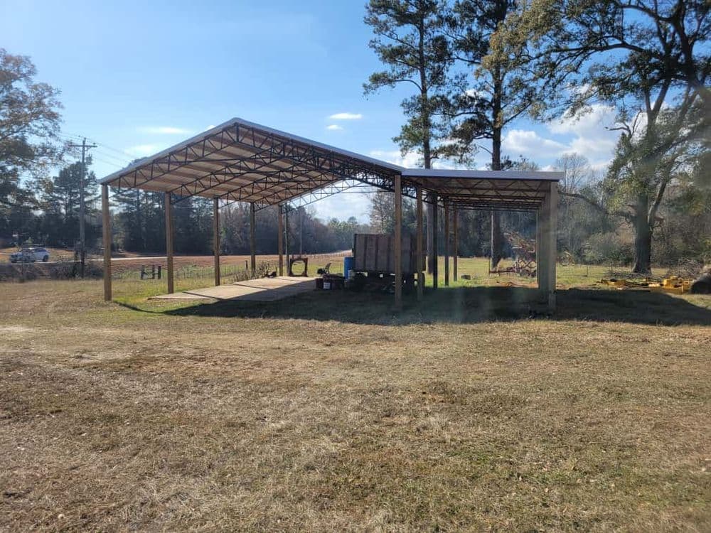 Open metal shelter on a grassy field with trees and power lines in the background.