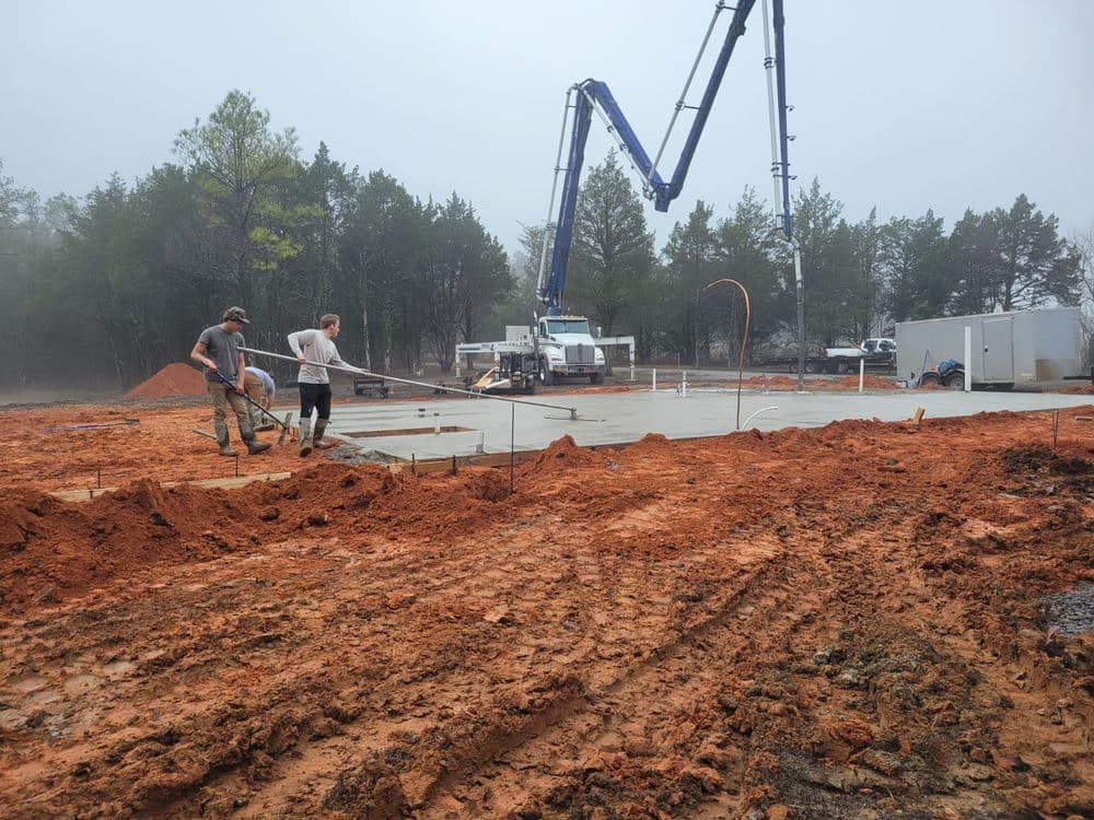 Construction workers pouring concrete on a foggy day at a building site with equipment.